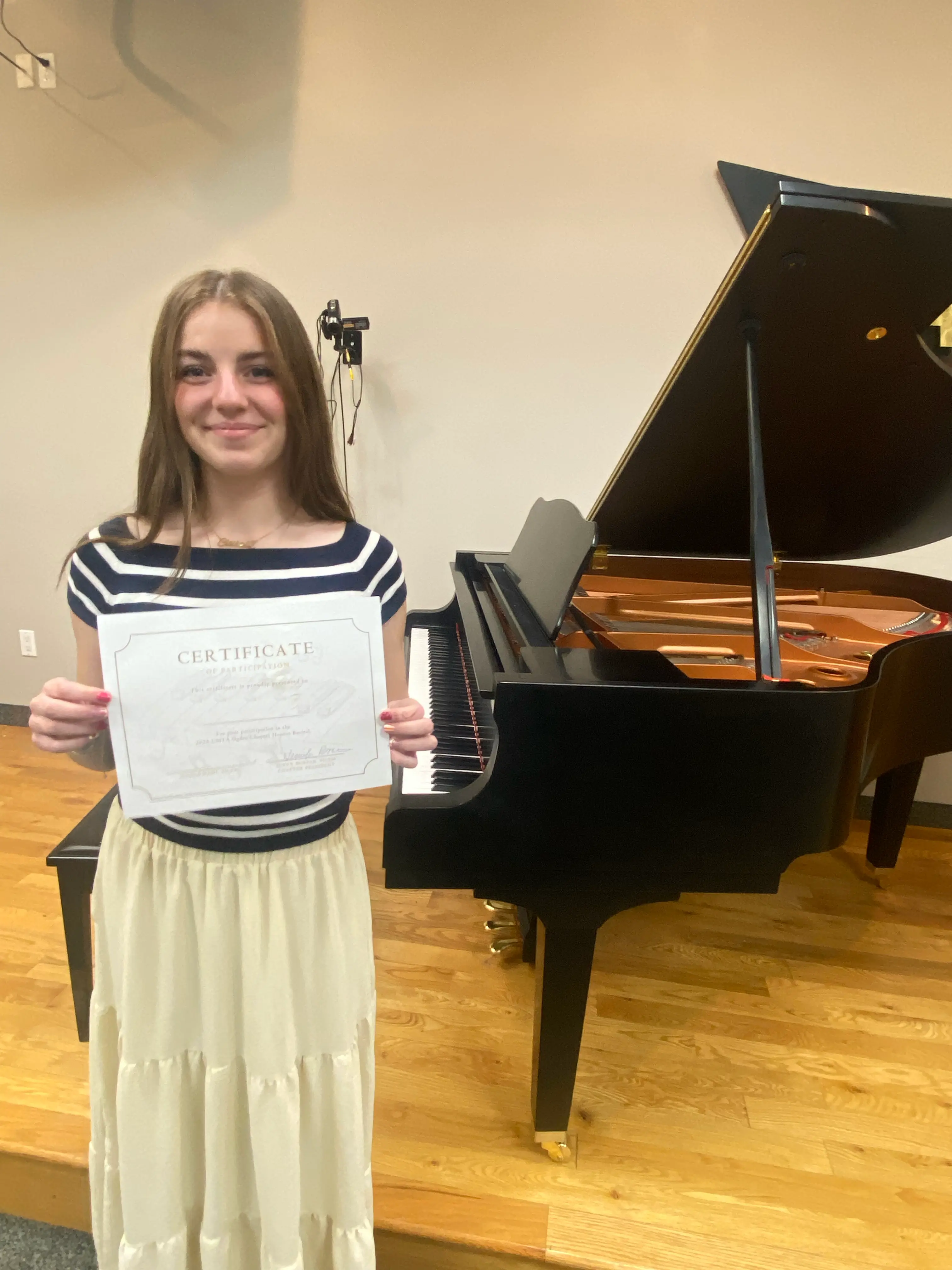 Student holding a certificate of participation beside a piano